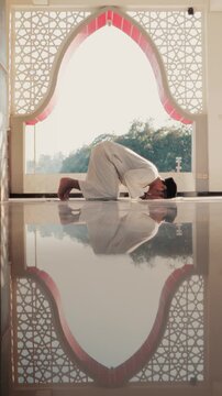 A Muslim man performing Islamic pray inside a mosque during Ramadan, a peaceful spiritual moment with beautiful mosque architecture and reflection on the polished floor.