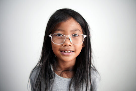 Portrait of a happy little Asian girl with eyeglasses smiling at camera with natural expression, cheerful childhood, positive lifestyle