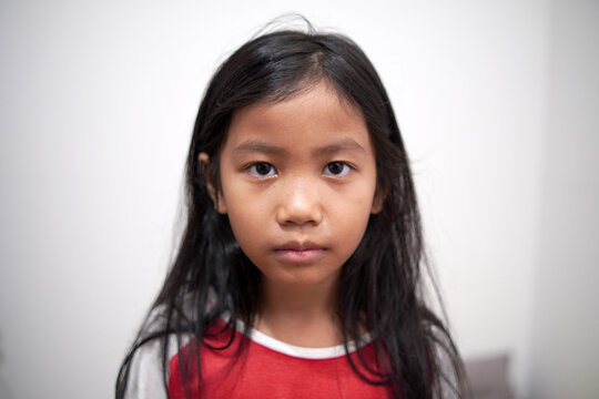 Little Asian girl looking at camera with neutral expression, standing indoors, blank stare, serious childhood face