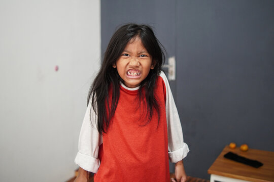 Angry Asian little girl growling and showing teeth with fierce expression. Portrait of stubborn child having a tantrum or feeling aggressive. Childhood behavior problems and frustration