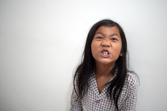 Angry Asian little girl in pajamas growling and showing teeth. Portrait of stubborn child with fierce facial expression and grumpy mood. Childhood behavior, aggression, and morning grouch concept