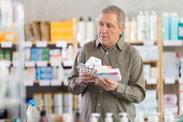 Elderly man with different packages of pills and medicines in a European pharmacy. Pensioner came...