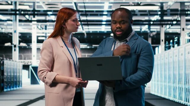 Server farm manager teaching intern to use laptop and optimize electronics during induction. Data center team leader and trainee using notebook to monitor system performance, camera B