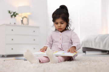 Fototapeta premium Cute little girl reading book on floor at home. Space for text