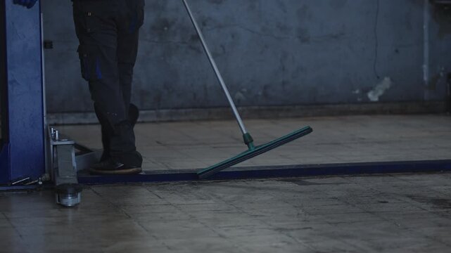 A skilled worker meticulously cleans the workshop floor using a broom and squeegee, ensuring a tidy and safe environment for everyone involved in their craft.