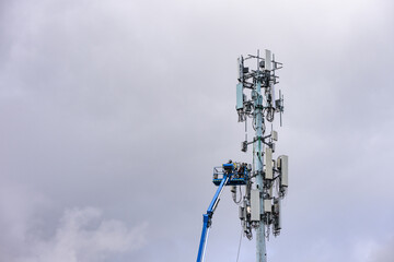 Obraz premium Boom truck lift backet with technician workmen raised up to antenna platform to perform maintenance, wireless mobile communication co-located cell sites on tall tower on cold winter day 