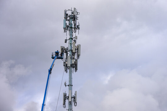 Boom truck lift backet with technician workmen raised up to antenna platform to perform maintenance, wireless mobile communication co-located cell sites on tall tower on cold winter day
