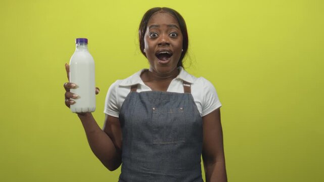 Woman in apron holds a milk bottle in hand and shows an open mouth surprised expression in studio; surprise wholesome.