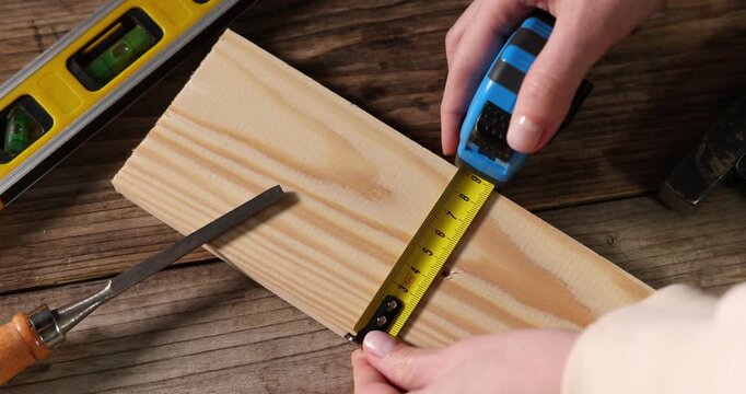 Woman measuring plank with tape at wooden table, above view. Camera moving in