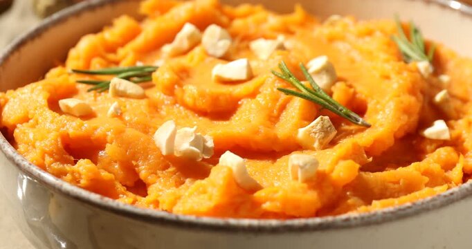 Delicious mashed sweet potato with cheese and rosemary in bowl on table, spinning. Closeup view