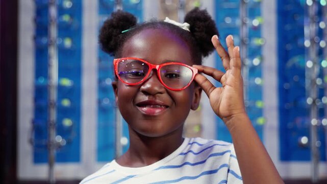 African girl child smiling while holding new red vision eyeglasses at optical shop