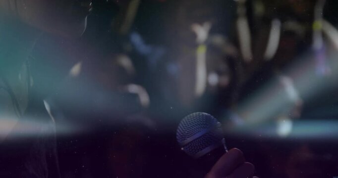 Camera clearing flare, female singer revealing profile, raising mic singing to crowd in concert