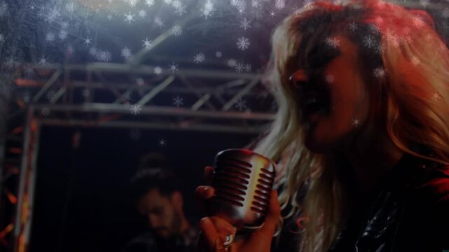 Singing female singer wearing dark jacket, holding vintage mic onstage with guitarist, snowflakes