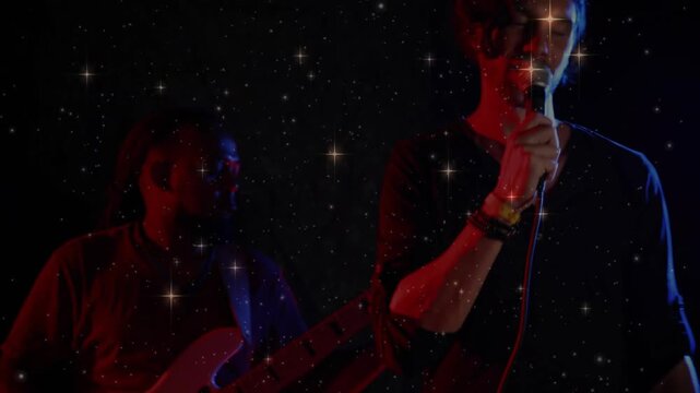 Singing singer wearing dark V-neck top moving wired mic closer on small stage, bassist playing bass