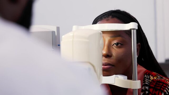 Young African woman having vision checked by optometrist using non-contact tonometer (NCT)
