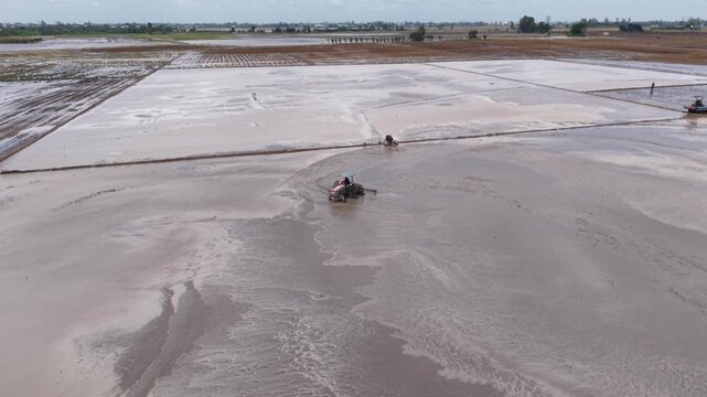 Aerial drone view of tractor leveling muddy rice field during farming season in Vietnam