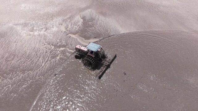 Aerial drone view of tractor leveling muddy rice field during farming season in Vietnam