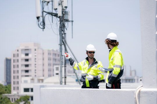 Two technician team talking collaboration working on rooftop building about communication transmitter system, development engineering and support maintenance, telecommunication and signal inspection.