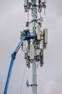 Boom truck lift backet with technician workmen raised up to antenna platform to perform maintenance, wireless mobile communication co-located cell sites on tall tower on cold winter day
