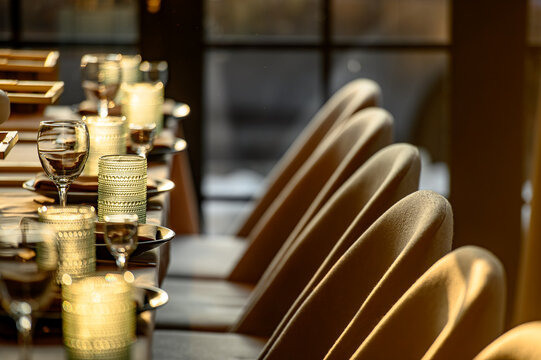 Row of chairs and set table in upscale restaurant. Perspective view of beige chairs and a dinner table with glasses in a warm, lit restaurant hall..