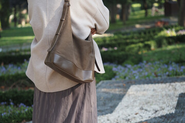 Woman stands in garden with bag on shoulder