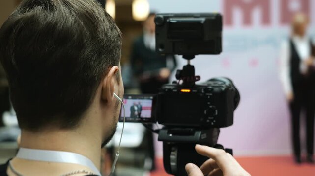 Behind the scenes of video production. Camera operator wearing earphone and monitoring audio while filming presentation at conference or business event.