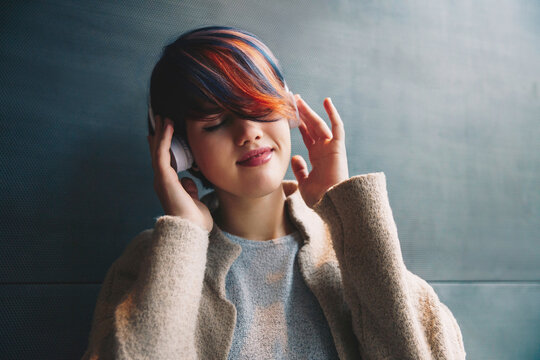Mental restcare. Technologies. Listening to music. Young woman with short colorful haircut in headphones is enjoying, her eyes are closed
