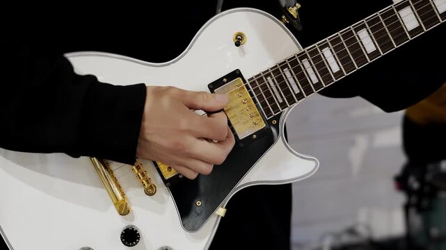 Close up of musician hand playing white electric guitar during performance. Concept of rock music band rehearsal live sound and musical instrument.