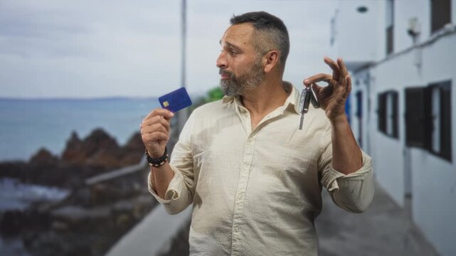Man holds creditcard in left hand and car key in right hand by a building on the seaside walkway; indecision choices.
