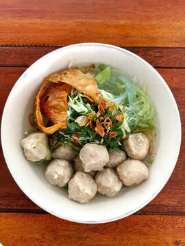 Indonesian Bakso Meatball Noodle Soup in White Bowl on Wooden Table