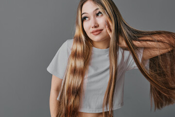 Young woman with long straight hair posing, wearing casual white t shirt against neutral...