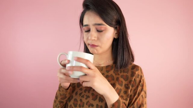 Close up of upset unhappy young Asian woman girl hold coffee cup in hands thinking reflection feels worried nervousness, isolated over light pink studio background.