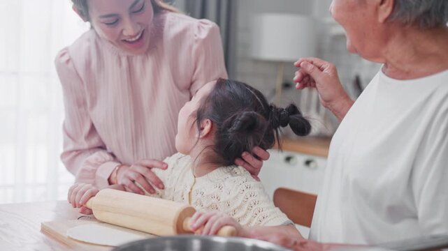Grandmother styles her granddaughter's hair while both she and the smiling mother guide the young girl through baking, sharing a heartfelt three-generation kitchen moment.