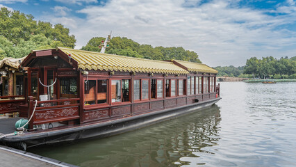 Obraz premium Beautiful Chinese boats are moored at the shore of the lake. Tiled roof, wood carvings, glass windows. Green vegetation, blue sky, clouds. China. Hangzhou. West Lake Xi Hu 