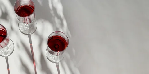 Top view of glasses filled with red wine on white table. Natural sunlight creates long graphic shadows and soft plant leaves silhouettes. Modern minimal summer mood banner, winery aesthetic, copyspace © yrabota