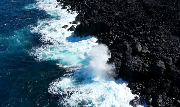 Aerial view captures the dynamic clash of powerful ocean waves against a rugged, dark volcanic rock coastline, a striking portrayal of nature's relentless force and beauty