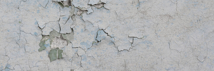 Obraz premium Peeling paint on the wall. Panorama of a concrete wall with old cracked flaking paint. Weathered rough painted surface with patterns of cracks and peeling. Grunge texture for wide panoramic background