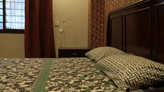 Neatly made bed with patterned bedding beside a window and curtains inside a modest bedroom interior