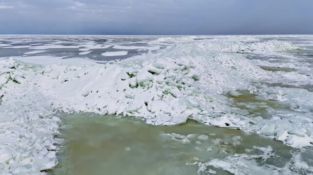 Drone view over chaotic ice shove ridge and slushy melt pool with hand-stacked ice towers in a surreal frozen coastal winter landscape.