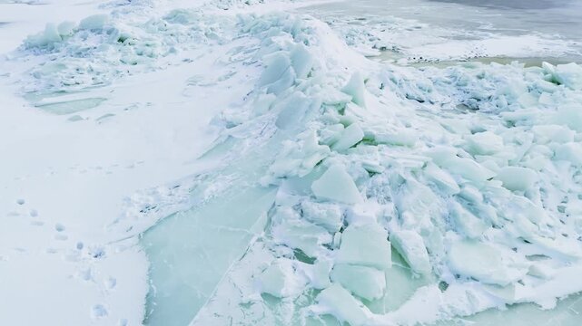 Drone glides over a jagged pressure ridge of broken frozen slabs beside snowy tracks, revealing unstable winter shoreline conditions and dramatic cold-weather textures.