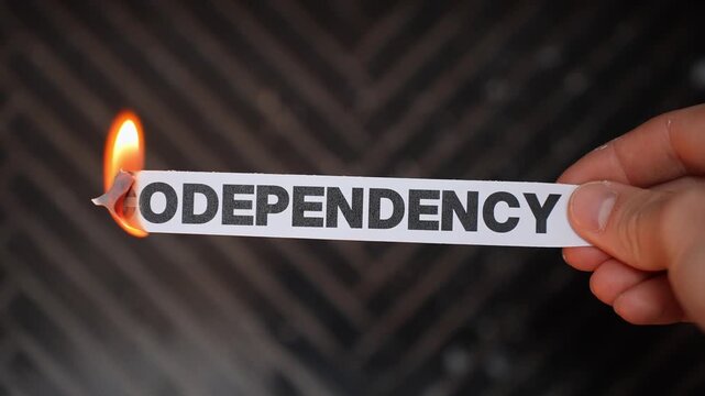 Hand burns a paper label reading &ldquo;CODEPENDENCY,&rdquo; symbolizing breaking unhealthy attachment&mdash;setting boundaries, independence, and relationship recovery. Dark background with copy space.