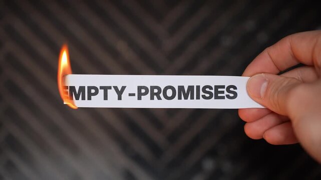 Close-up hand burns a paper label reading &ldquo;EMPTY-PROMISES,&rdquo; symbolizing betrayal, lies, and broken commitments. Dark background with copy space for business or relationship conflict themes.