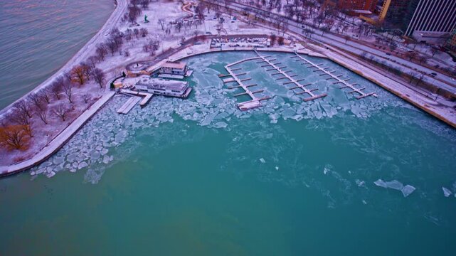 Cinematic drone view of frozen Lake Michigan harbor with urban skyline near Chicago Loop in wintertime.