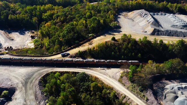 Aerial tilt down across of quarry railway cars transporting aggregate as semi truck drives on dirt road