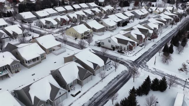 Aerial drone flyover of snow covered suburban neighborhood with rows of residential houses, winter streets and rooftops in Pennsylvania, USA during cold overcast winter day.