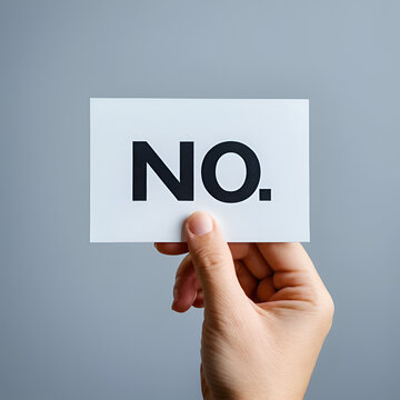 A person's hand holding a small sign with a bold "NO" written on it, symbolizing setting boundaries and embracing assertive communication in daily life.