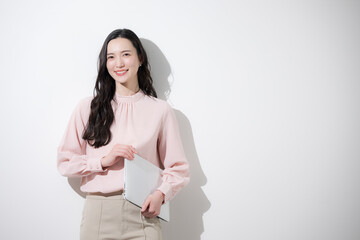 Fototapeta premium 白背景でパソコンを持つかわいいオフィスカジュアルの日本人女性のカメラ目線の笑顔 自信や成長やポジティブで多幸感あふれる春色ビジネスイメージ