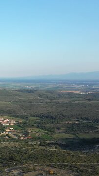 Scenic aerial view of Opoul Perillos village surrounded by green fields and Mediterranean countryside under a clear blue sky in southern France.