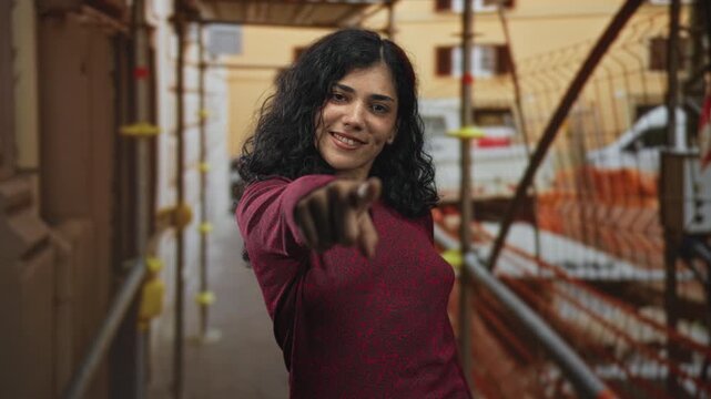 Woman points finger to camera amid building scaffolding and safety netting; confidence empowerment determination.