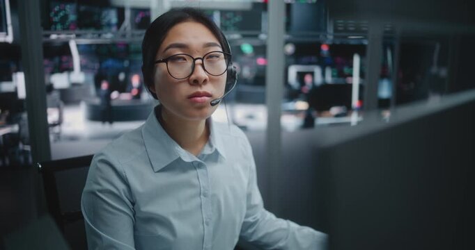 Young Asian Financial Analyst Consulting on Headset in Futuristic Trading Hub. Tech Savvy Female Broker Wearing Headset, Engaged in Deep Data Analysis. Key Decision Maker in Global Financial Market.